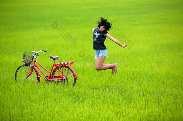 快乐的女孩在稻田里骑自行车跳来跳去