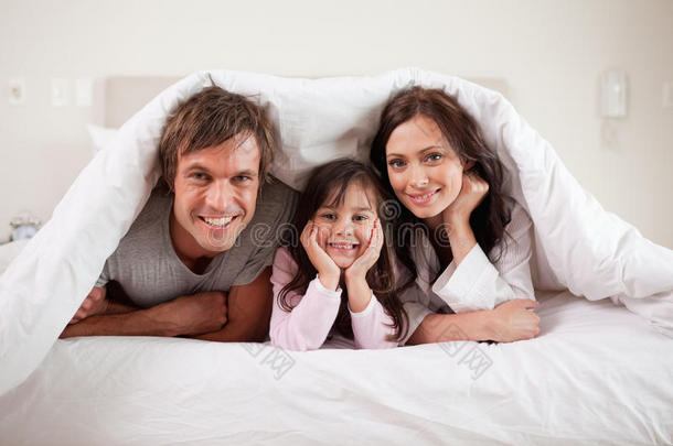 带着微笑的父母和女儿躺在羽绒被下