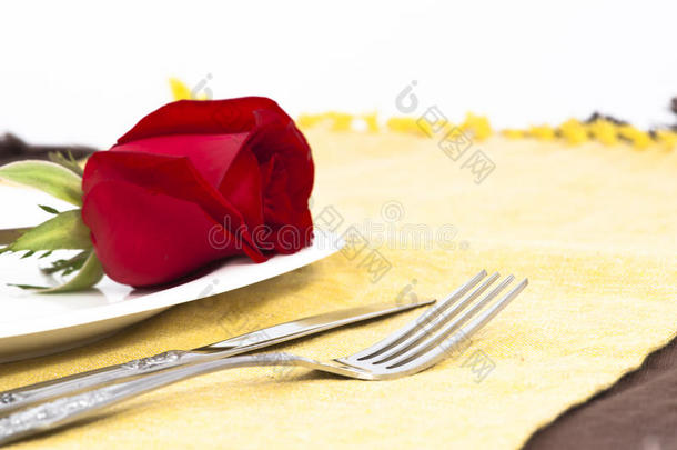 白盘子上的红玫瑰和餐具
