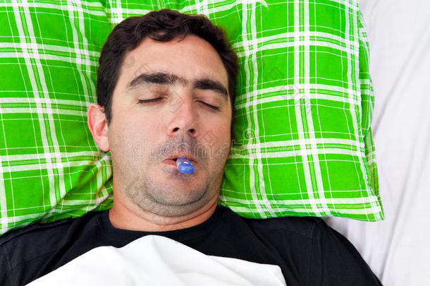 生病的西班牙裔男子躺在床上拿着温度计