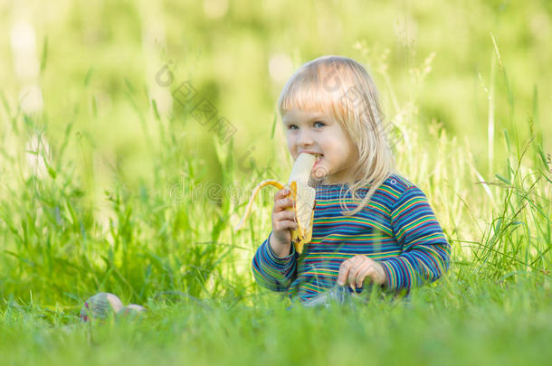 可爱的宝宝坐在公园的草地上吃香蕉