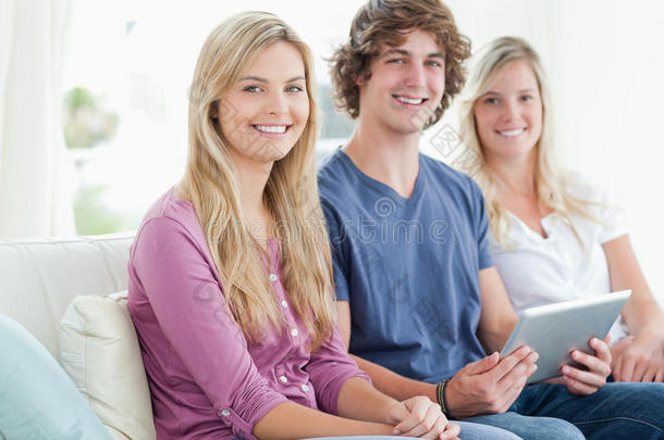 三个面带微笑的人坐在沙发上，手里拿着一块平板电脑