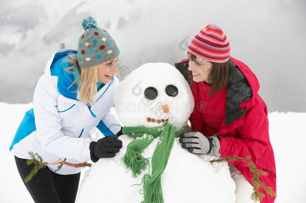 两个女朋友在滑雪度假时堆雪人