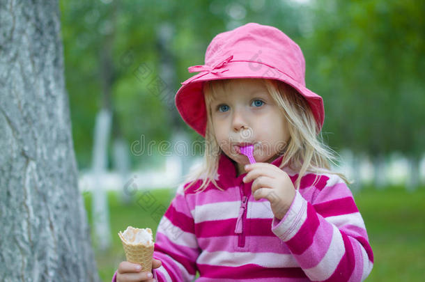 戴红帽子的可爱女孩在树下吃冰淇淋