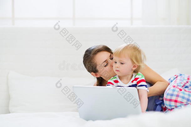 <strong>妈妈亲吻</strong>她的现代<strong>宝宝</strong>在笔记本电脑上工作