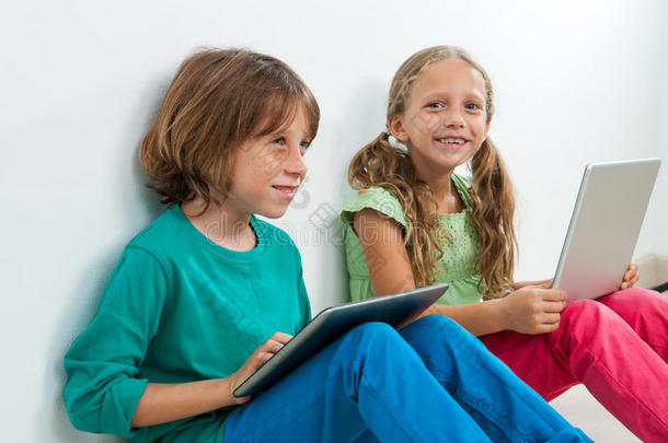 两个孩子坐在笔记本电脑和数字平板电脑前。