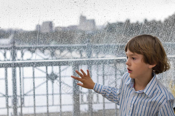 微笑的男孩看着窗外的雨