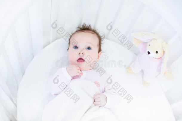 可爱的小女孩，穿着白色的圆婴儿床，带着粉色的小兔子玩具