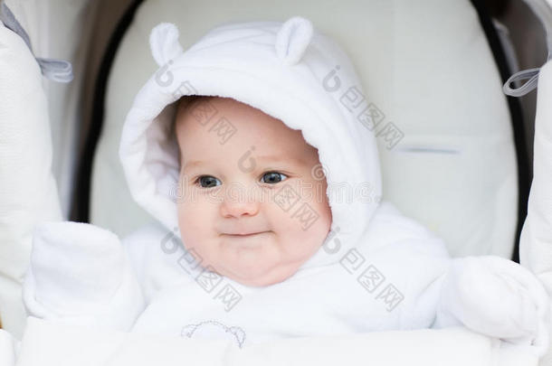 在寒冷的冬天，戴着泰迪熊帽子的可爱的小宝宝坐在白色的婴儿车里