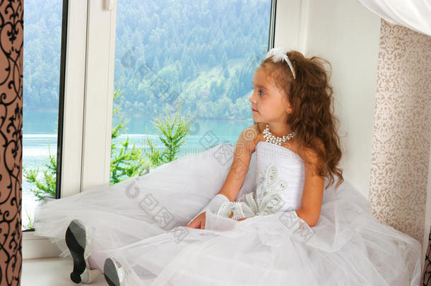 一个穿着白色连衣裙的优雅女孩坐在窗台上