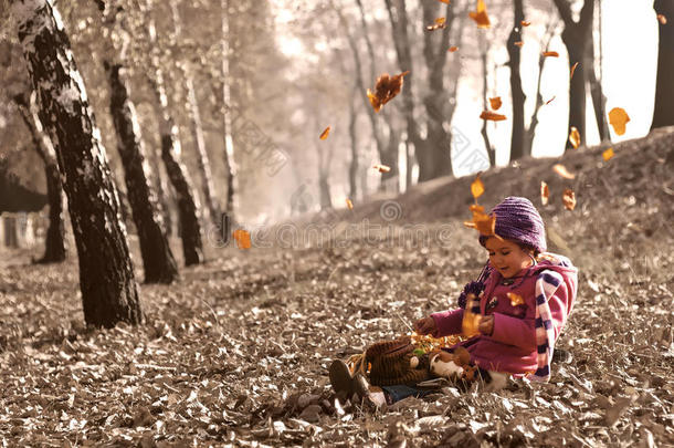 可爱的女孩坐在秋天的落叶上，<strong>树叶飘落</strong>，玩弄着洋娃娃