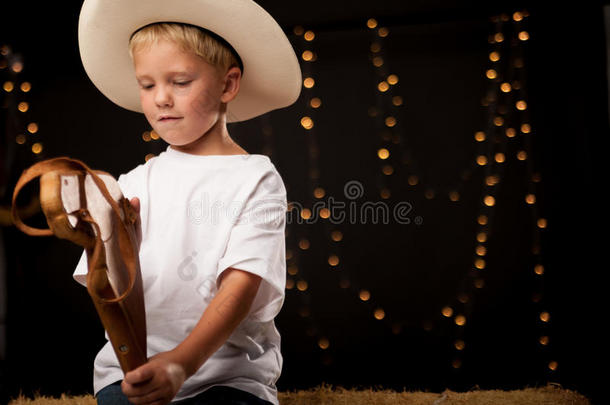 一个年轻的牛仔坐在干草包上，手里牵着一匹<strong>骏马</strong>