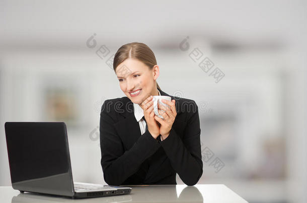 微笑的女商人坐在笔记本电脑前，<strong>端着</strong>咖啡和茶杯
