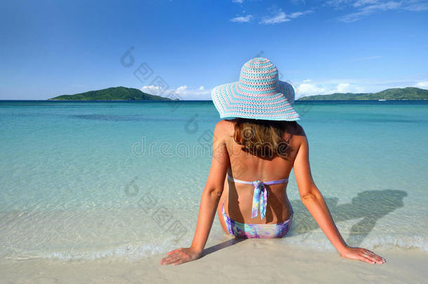一个戴着夏天帽子的女孩躺在沙滩上，看着背景上的天空
