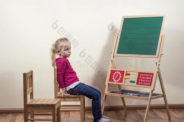 一个小女孩独自坐在黑板前。
