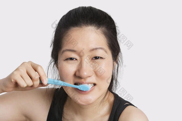 一位年轻女子在浅灰色背景下刷牙的画像