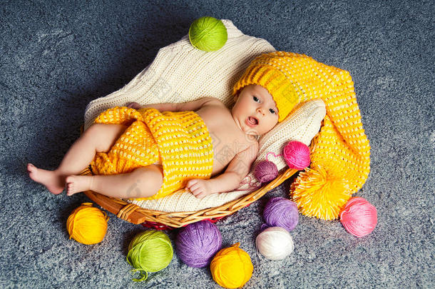 打呵欠的婴儿躺在篮子里。编织用的纱线周围。
