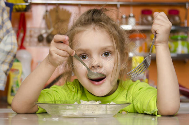 一个四岁的女孩坐在厨房的桌子旁用叉子和勺子吃饭