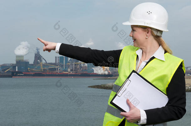 女巡视员头戴安全帽，穿着安全背心，指着工业现场