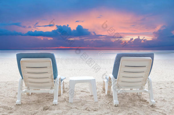 一对对椅子沙滩上的白色沙滩上，昏暗的天空背景