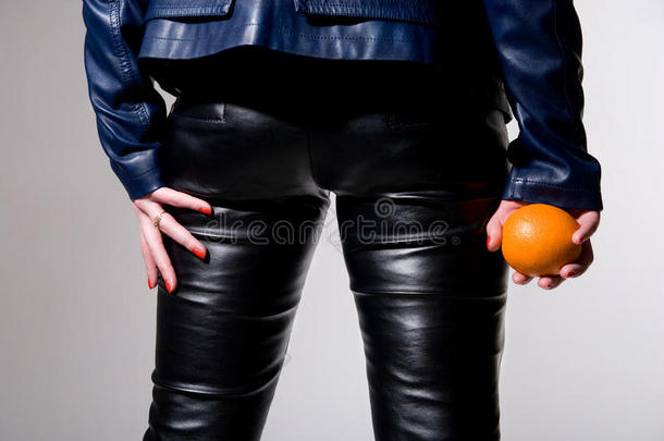 穿黑色<strong>皮裤</strong>的女孩手里拿着一个橘子。