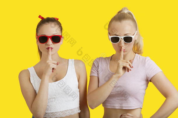 两个调皮的年轻女子的画像，嘴唇上有手指，背景是黄色