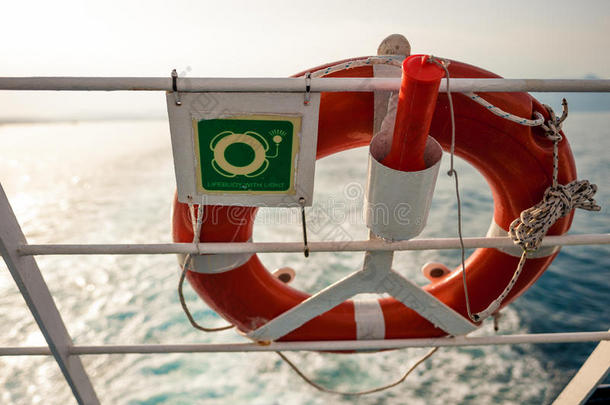 带标志的救生圈在渡轮围栏上，太阳和大海在后面