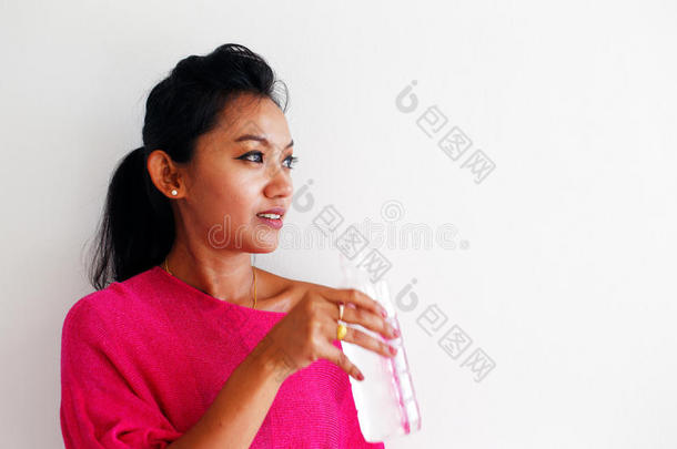 一个年轻的女人喝着水站在白色的墙上