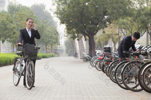 中国北京，年轻的商务人士在人行道上停放自行车和打电话