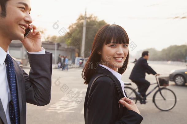 两个微笑的年轻商人走在北京的大街上，打电话