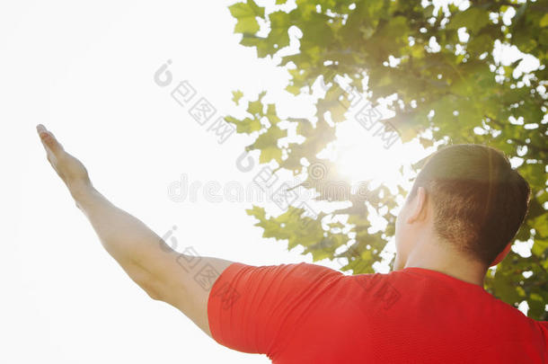 在中国北京，年轻肌肉男伸展在树上，手和手臂向天空和太阳升起的后视图