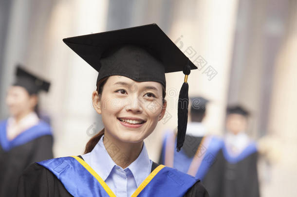 身着毕业礼服的微笑的年轻女毕业生和背景中的研究员