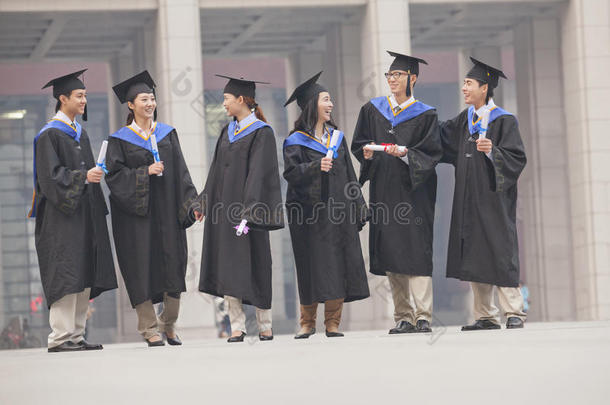 一批身着毕业礼服，手拿毕业证站着说话的研究生