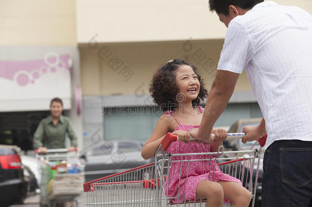 女儿坐在购物车里，父亲推着，在超市门口