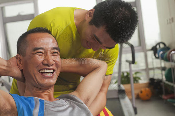 微笑的男人和他的教练一起锻炼，做仰卧<strong>起坐</strong>