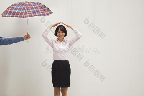 年轻的女商人双手举过头顶，同事给她撑伞