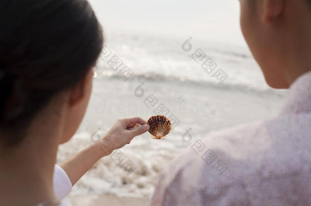 站在沙滩上看贝壳的年轻夫妇，肩上的风景