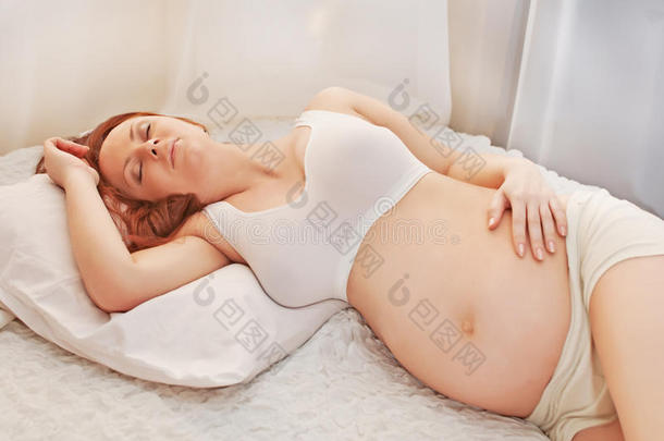 怀孕的金发女人在沙发上放松，看书，做梦，