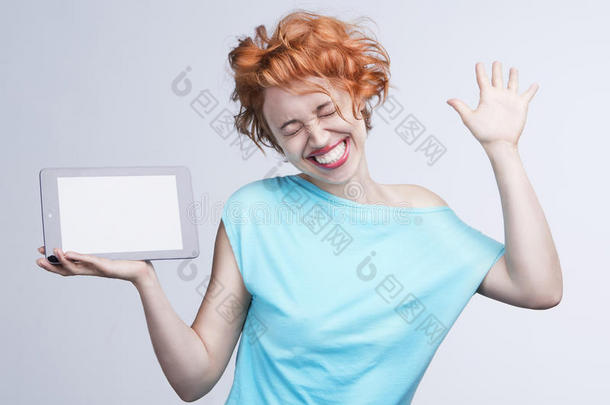 情绪激动的红发女孩拿着平板电脑，高兴地跳舞、跳跃、大笑。