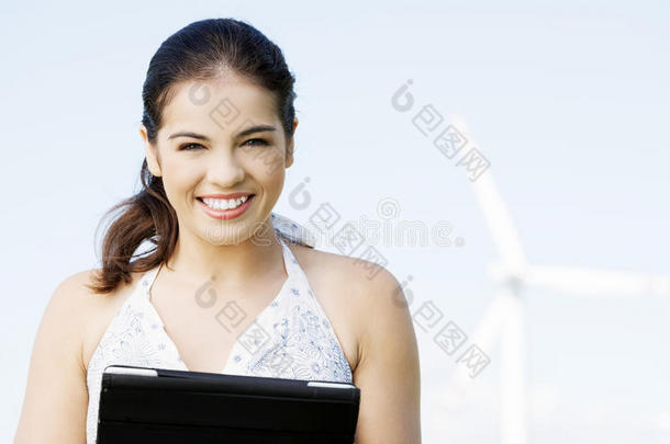 一个十几岁的女孩，在风力发<strong>电机</strong>旁边拿着平板<strong>电脑</strong>。