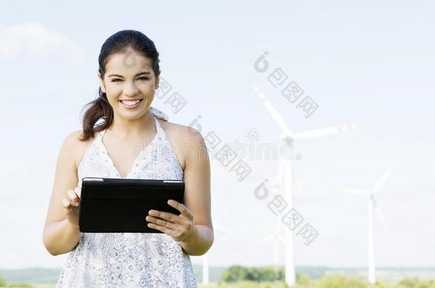 一个十几岁的女孩，在风力发<strong>电机</strong>旁边拿着平板<strong>电脑</strong>。