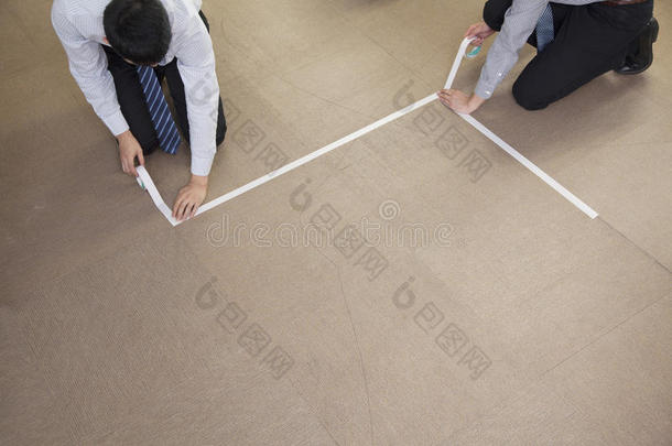 两个<strong>年</strong>轻的商人在办公室里用胶带把地板捆扎起来