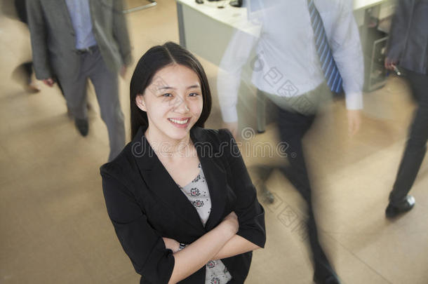 年轻的女商人在办公室微笑，商人在她周围走动