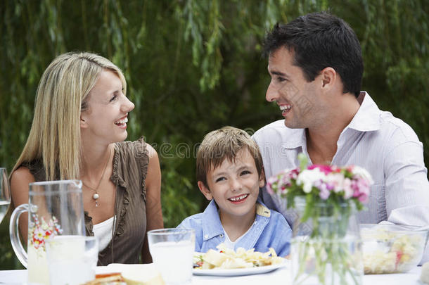 快乐的父母和儿子坐在花园的餐桌旁