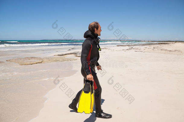 男潜水员，穿着潜水服，戴着潜水面罩，脚蹼在沙滩上