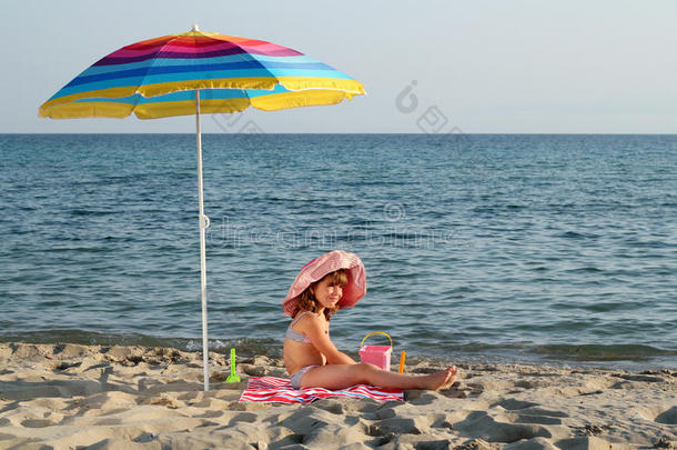 坐在沙滩遮阳伞下的小女孩