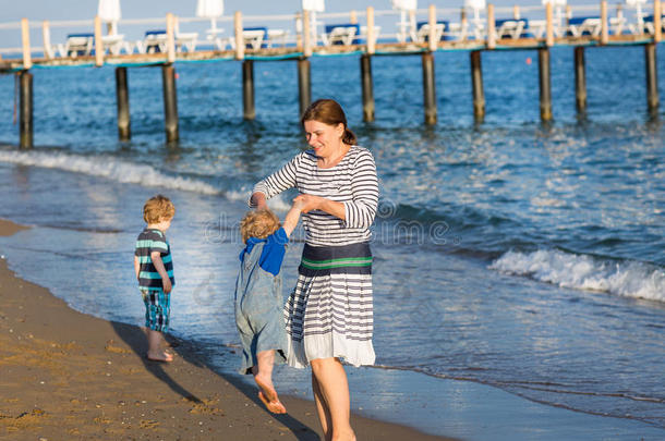 快乐的母亲和两个在沙滩上散步的小孩