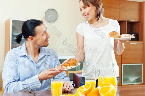 微笑的女人端着羊角面包和炒鸡蛋她的男人