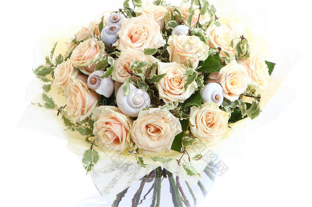用奶油玫瑰和贝壳做成的插花，透明的玻璃花瓶。隔离在白色背景上。花卉成分。