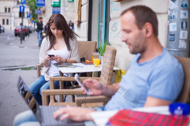 一个女人拿着手机，一个男人拿着笔记本和手机坐在咖啡馆里。